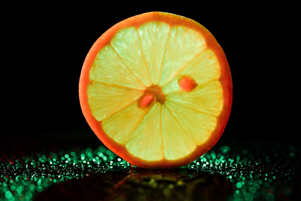 schijfje citroen met neon achtergrondverlichting op zwarte achtergrond - Foto, afbeelding