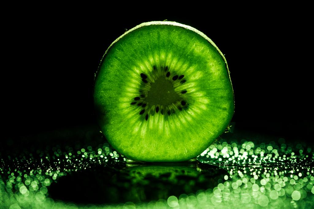 plakje kiwi fruit op zwarte achtergrond met neon groene achtergrondverlichting - Foto, afbeelding