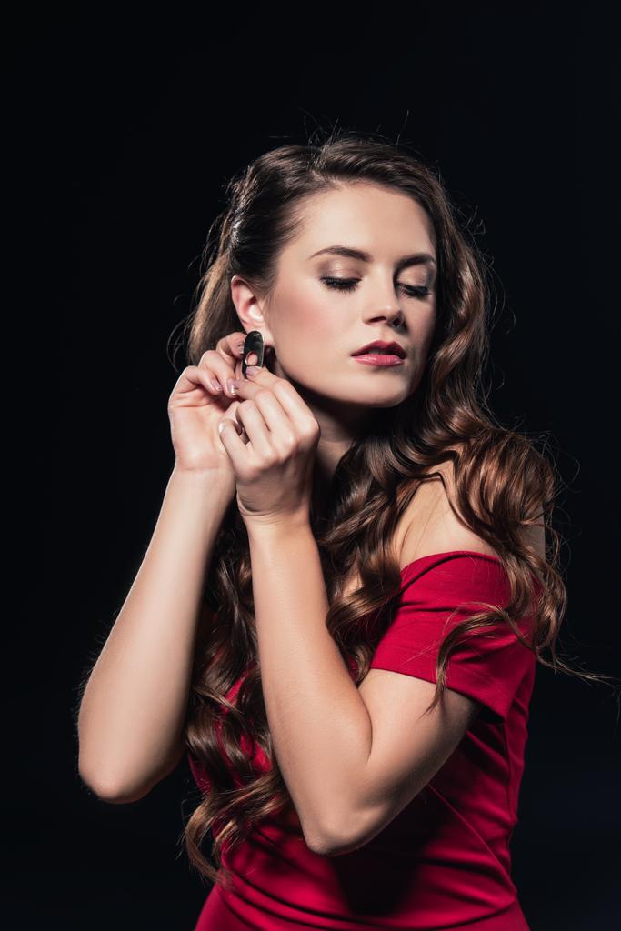 woman in red dress putting on earring isolated on black - Photo, Image