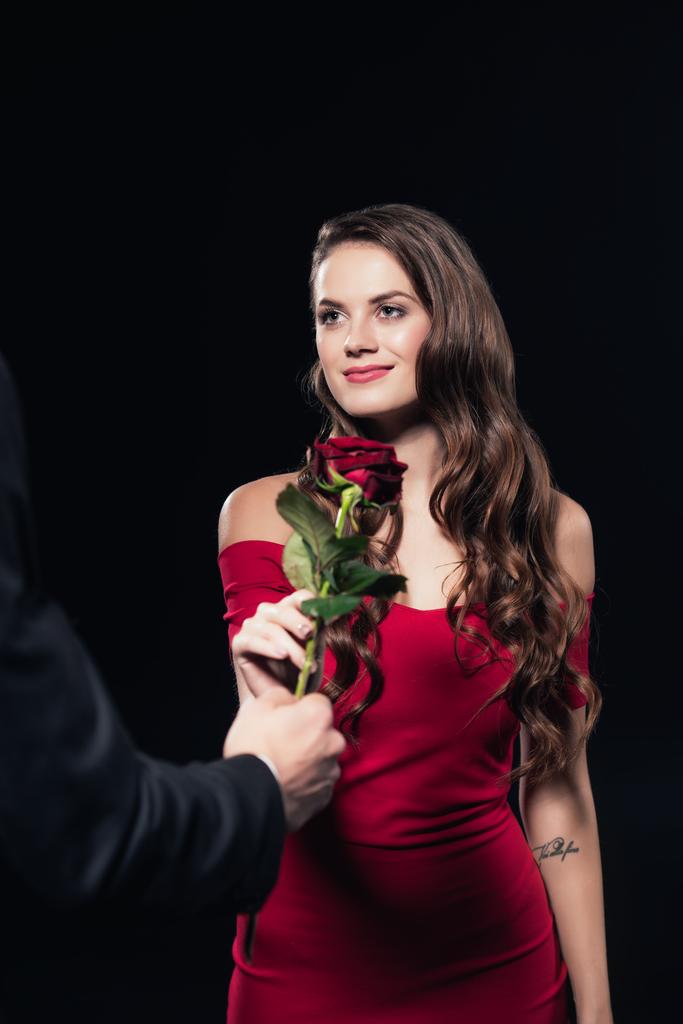 мужчина, представляющий розу красивой улыбающейся женщине в красном платье, изолированном от черного
 - Фото, изображение