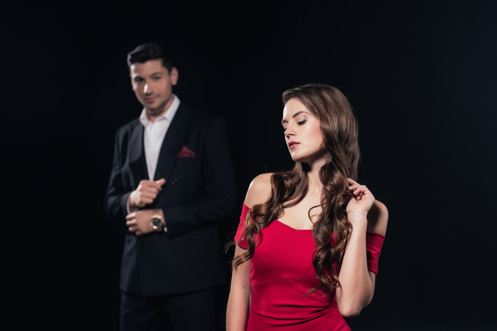 селективное внимание красивой женщины в красном платье с мужчиной на заднем плане изолированы на черном
 - Фото, изображение