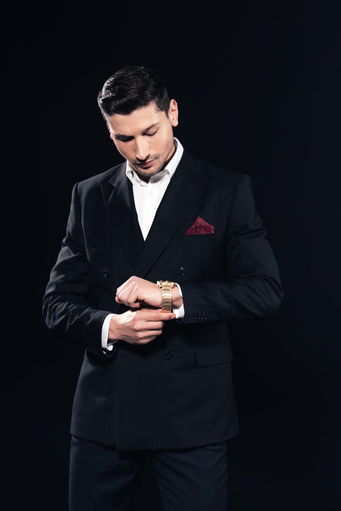Сосредоточенный человек в костюме надевает часы изолированные на черный
 - Фото, изображение