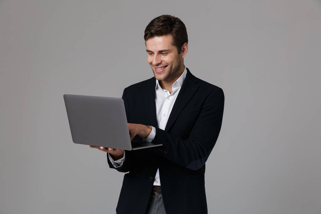 Kuva tyytyväinen liikemies 30s puku riemuitsee käytettäessä kannettavaa eristetty yli harmaa tausta
 - Valokuva, kuva