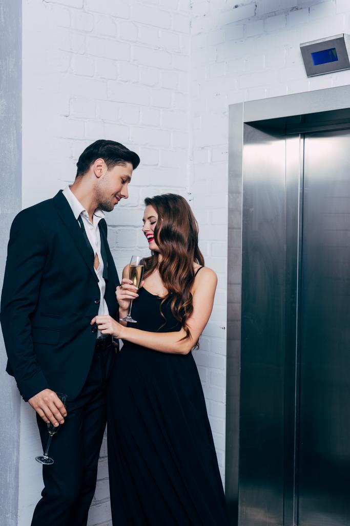 pareja feliz sosteniendo copas de champán, hablando y esperando el ascensor
 - Foto, imagen