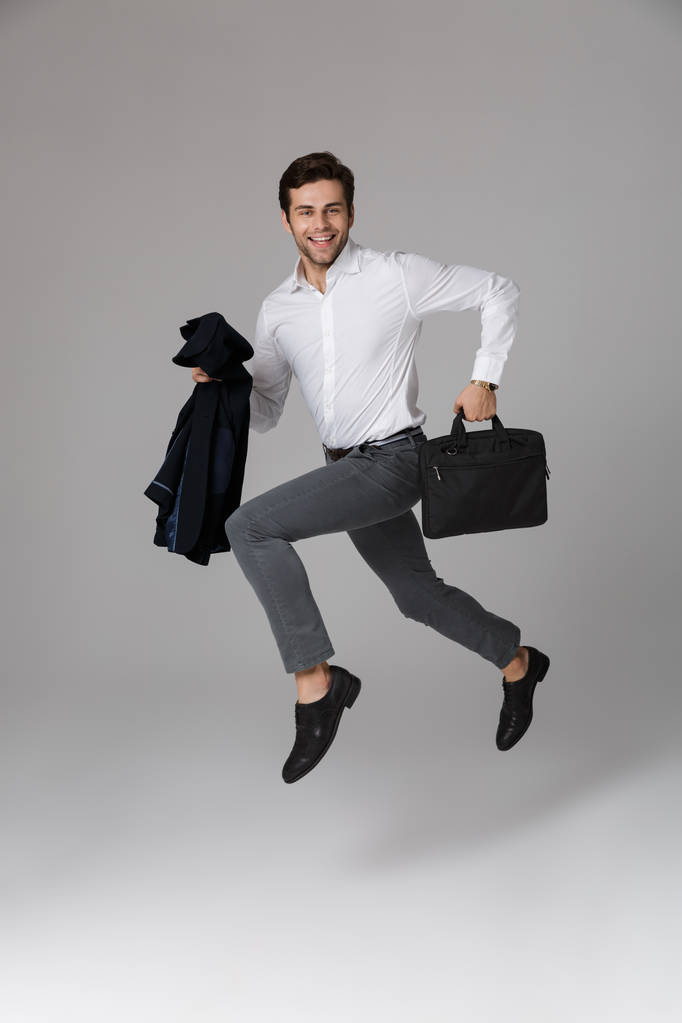 Full length image of excited man 30s in business suit running with bag and jacket in hands isolated over gray background - Photo, Image