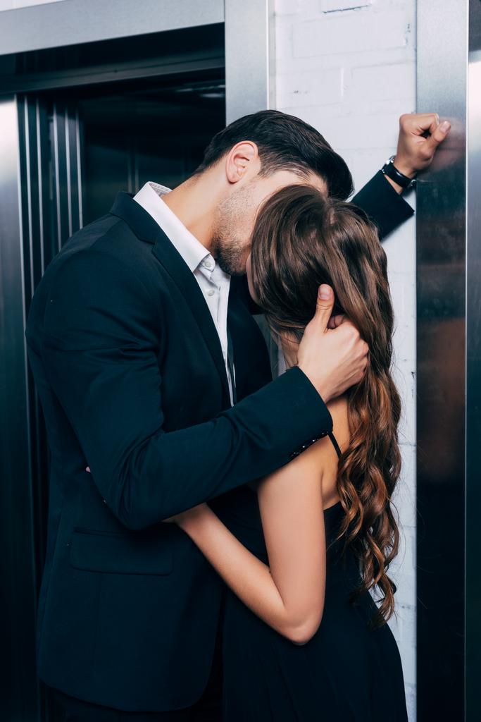 Mann im Anzug küsst und umarmt Frau in Fahrstuhlnähe leidenschaftlich - Foto, Bild