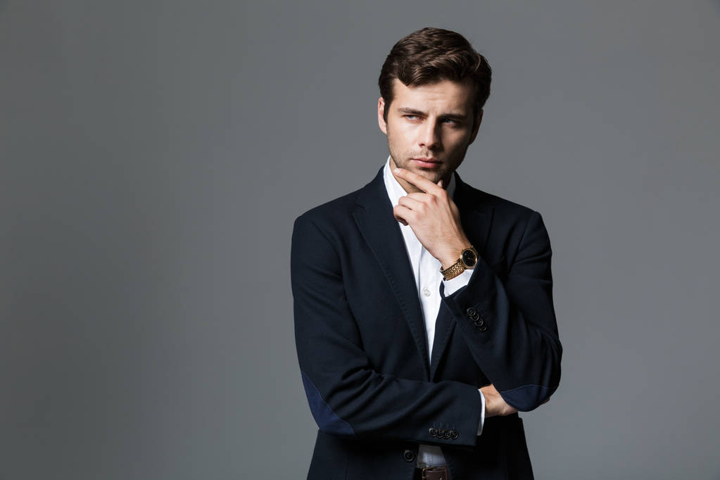 Close up retrato de um jovem empresário pensativo vestido de terno isolado sobre fundo cinza, olhando para longe
 - Foto, Imagem