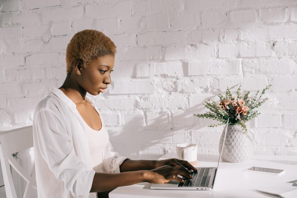 Afrikalı-Amerikalı kadın laptop beyaz mutfak yazmaya konsantre  - Fotoğraf, Görsel