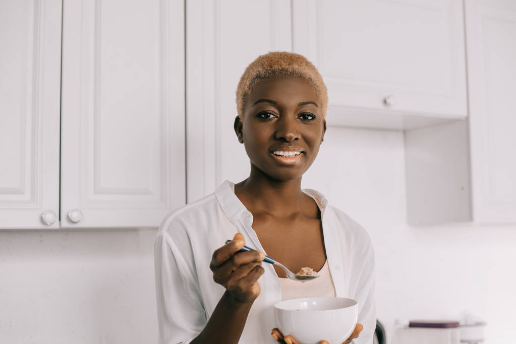 glückliche afrikanisch-amerikanische Frau mit Löffel und Schüssel mit Cornflakes - Foto, Bild