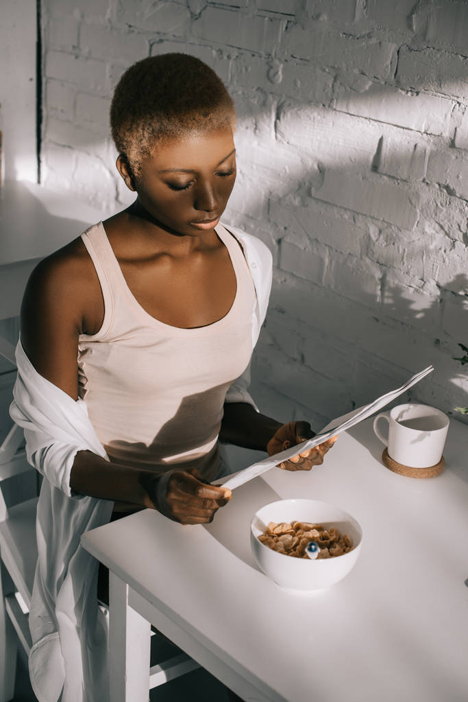 prachtige Afrikaanse Amerikaanse vrouw lezen van de krant in witte keuken  - Foto, afbeelding