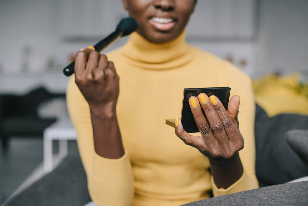 vue recadrée de femme afro-américaine appliquant de la poudre avec un pinceau cosmétique
  - Photo, image