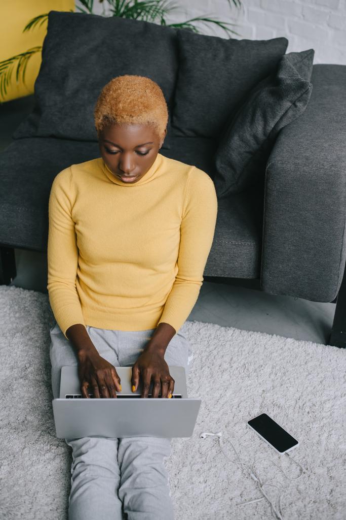 afrikai-amerikai nő ül a szőnyegen, és használ laptop  - Fotó, kép