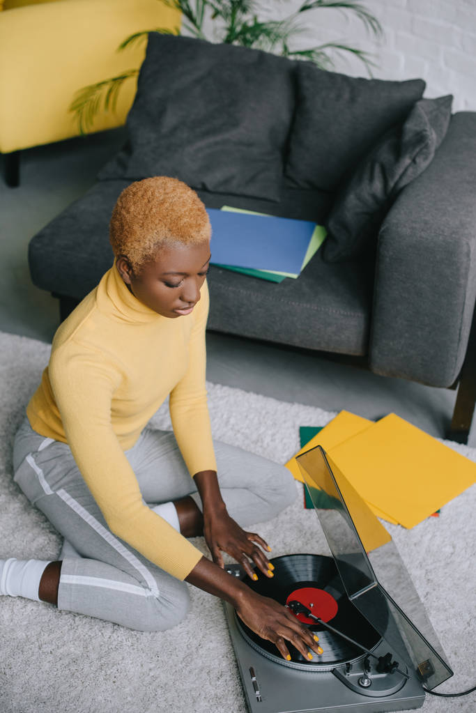 attraktive Afroamerikanerin benutzt Plattenspieler auf Teppich - Foto, Bild