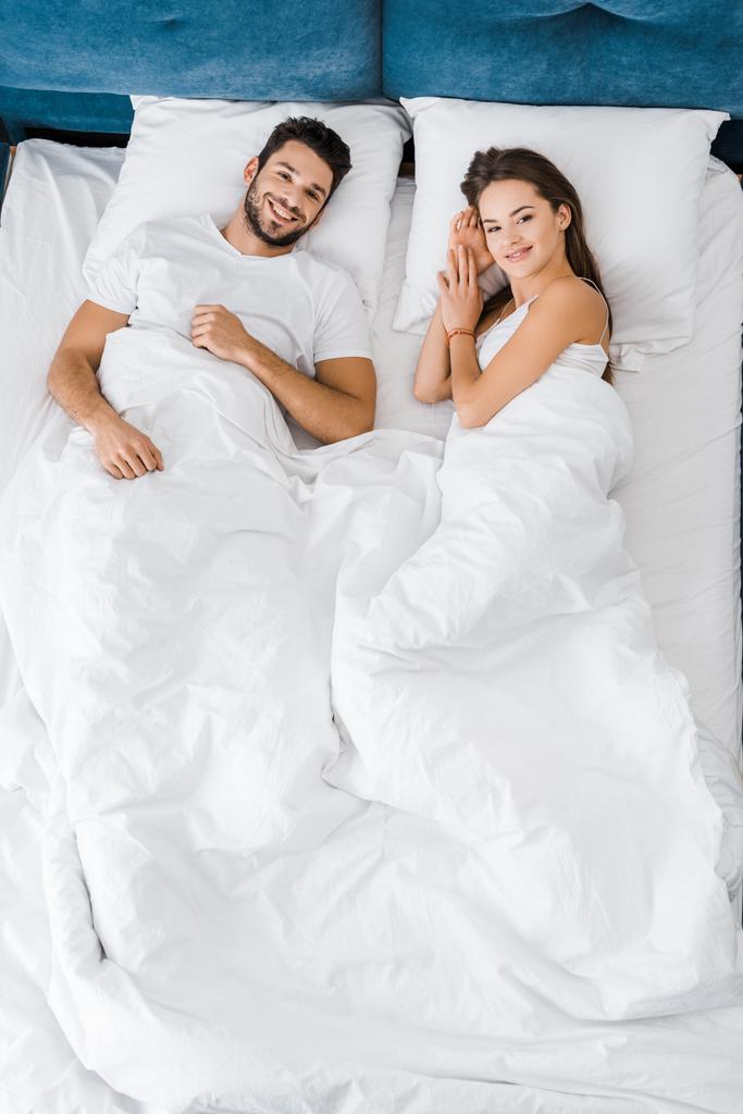top view of cheerful smiling couple lying in bed together - Photo, Image