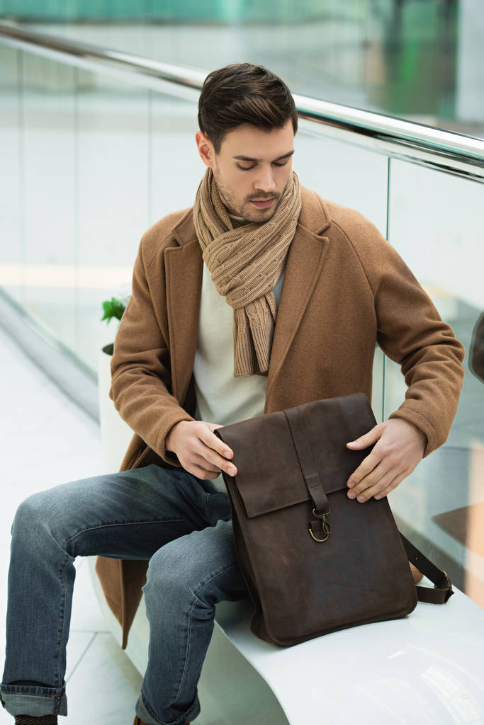 hombre guapo sosteniendo bolsa y sentado en el banco
 - Foto, Imagen