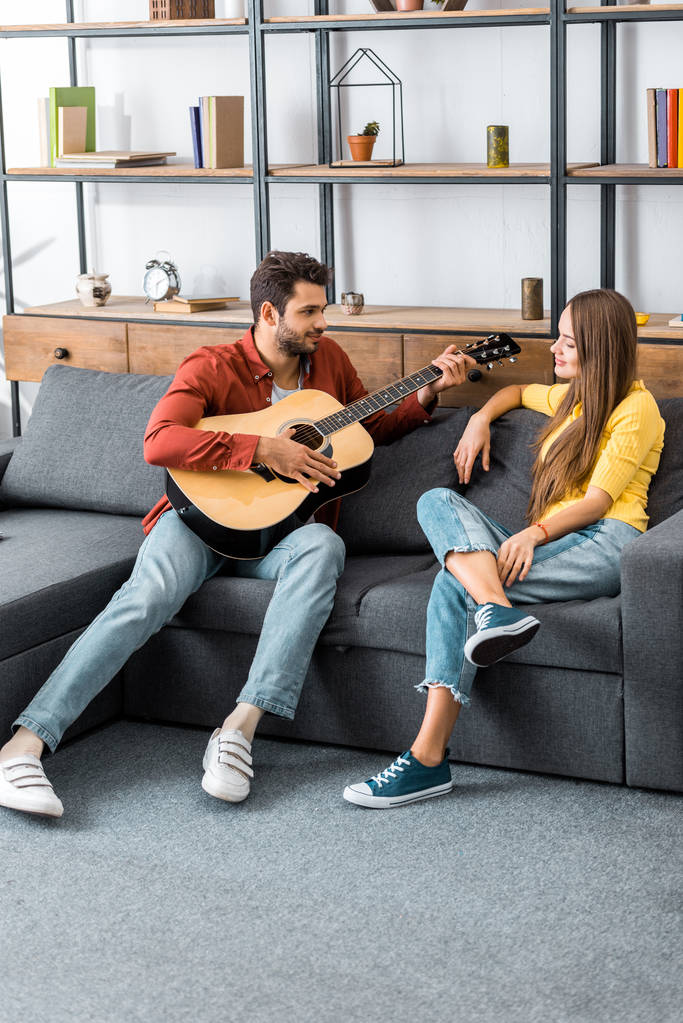 молодий красивий чоловік грає на гітарі для дівчини у вітальні
 - Фото, зображення