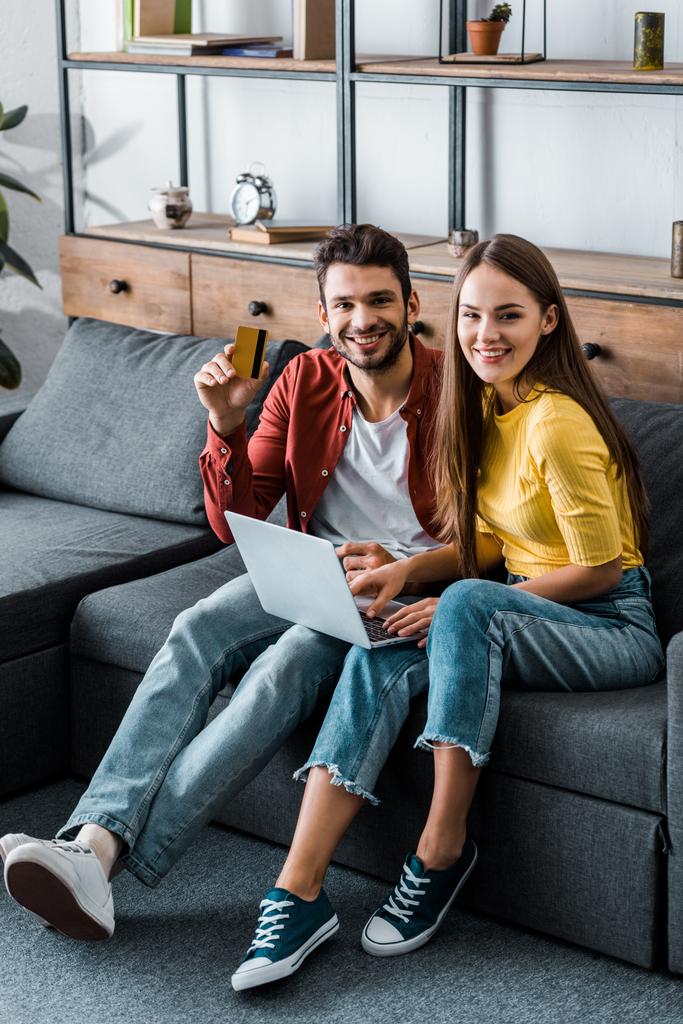 cheerful boyfriend and girlfriend doing online shopping on sofa in living room - Photo, Image