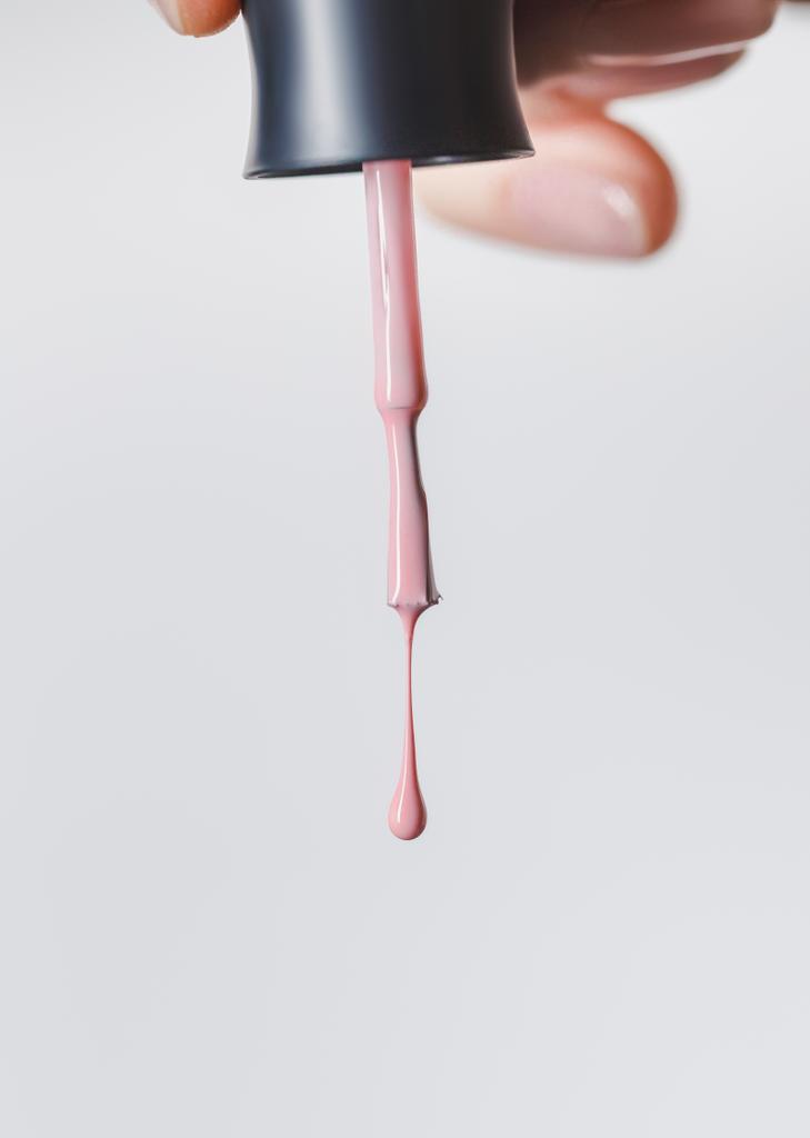 vista parcial de la mujer sosteniendo cepillo con esmalte de uñas rosa aislado en gris
 - Foto, Imagen