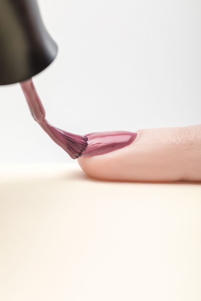 блестящий фиолетовый лак для ногтей на ногтях женщины на сером фоне
 - Фото, изображение