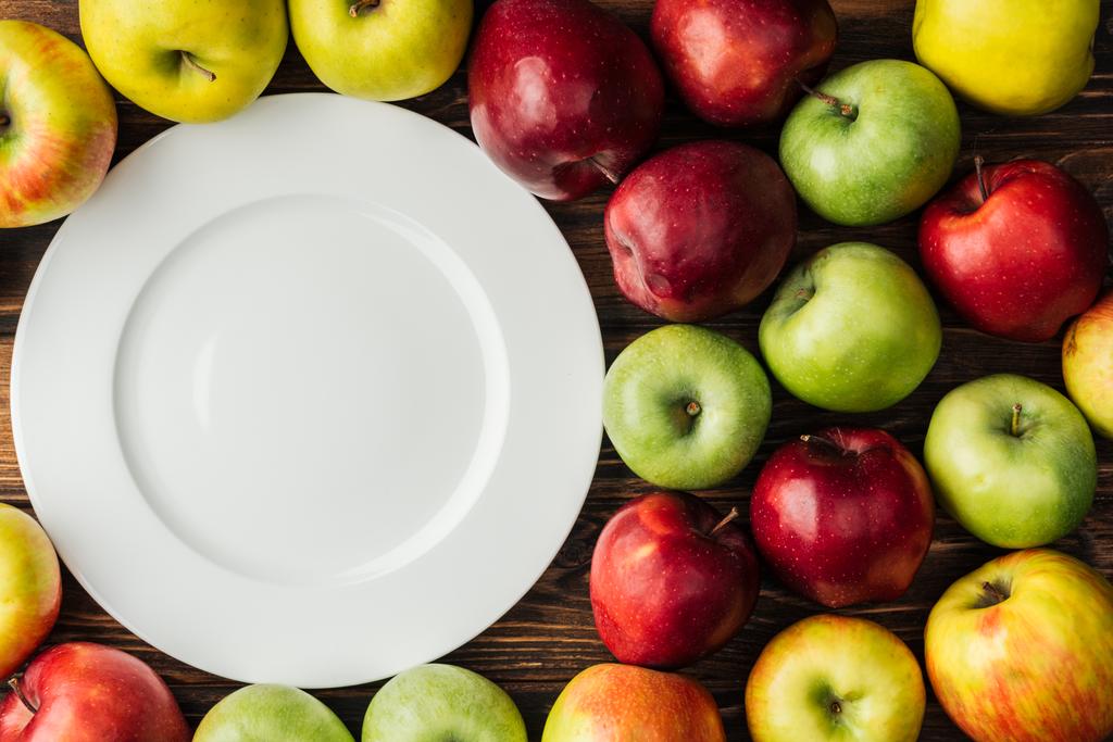 木製のテーブルに白いプレートと色とりどりのりんごのトップ ビュー - 写真・画像