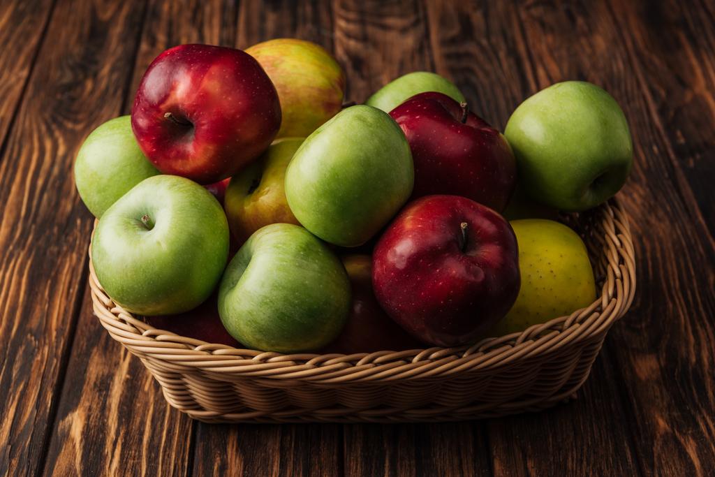 panier en osier avec de délicieuses pommes rouges, vertes et jaunes sur table en bois
 - Photo, image