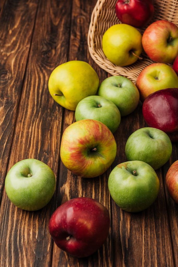 porozrzucane jabłka wielobarwny i Wiklinowy kosz na drewnianym stole - Zdjęcie, obraz