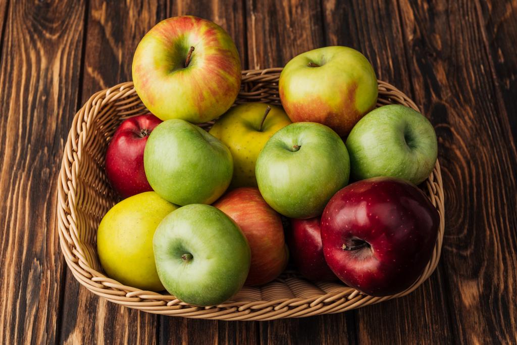 Cesta de mimbre con manzanas maduras multicolores sobre mesa de madera rústica
 - Foto, imagen