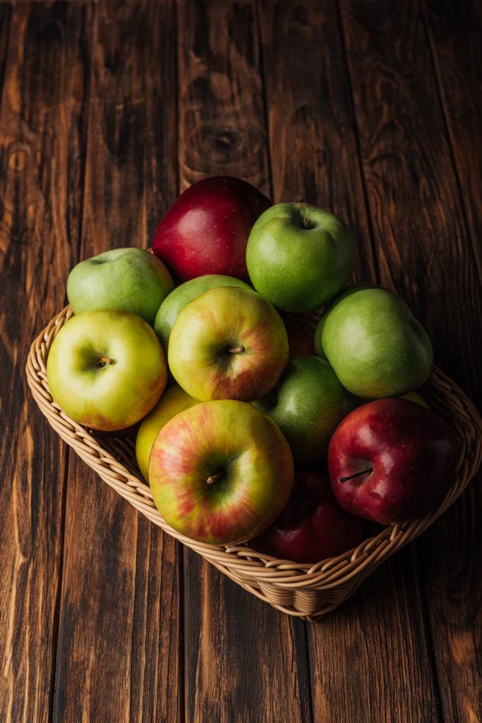 red, green and golden apples in wicker basket on rustic wooden table - Photo, Image