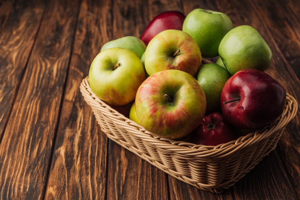ripe multicolored apples in wicker basket on rustic wooden table - Photo, Image
