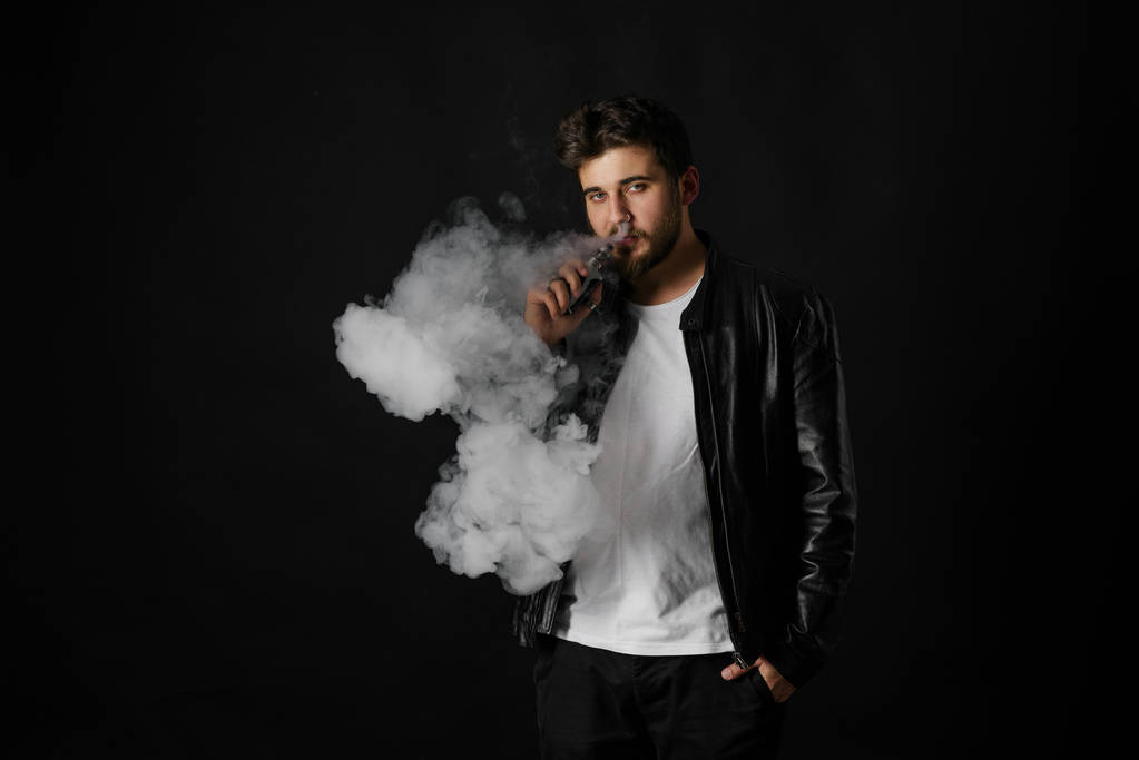 Człowiek z vaping mod wydechu steam w studio czarne tło. Brodaty facet e-papierosa rzucić tytoniu. Pary i alternatywnych koncepcji darmo palenia nikotyny - Zdjęcie, obraz