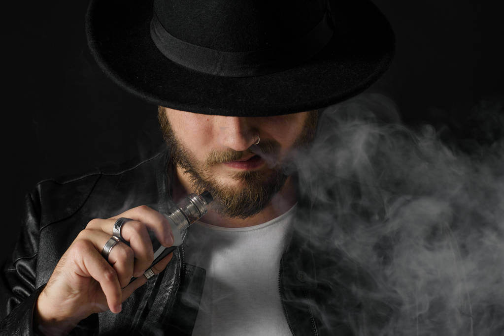 Férfi vaping mod exhaling steam a stúdió-fekete háttér. Szakállas fickó e-cigaretta dohányzásról leszokni a dohány. Gőz- és alternatív nikotin szabad dohányozni koncepció - Fotó, kép
