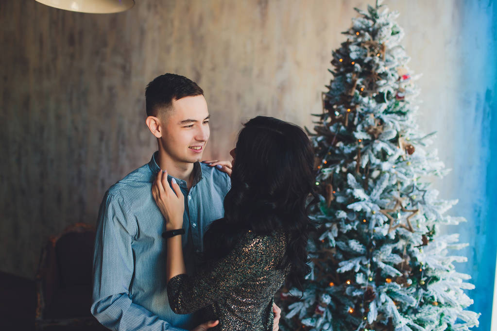 A man and a woman are dancing against the background of a Christmas tree. Beautiful happy young family celebrating Christmas together. Lovers on the New Year together in an apartment in the Loft style - Photo, Image