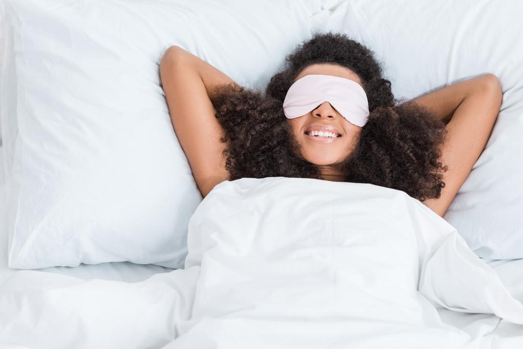 happy african american girl with eyes covered by sleeping blindfold in bed during morning time at home - Photo, Image