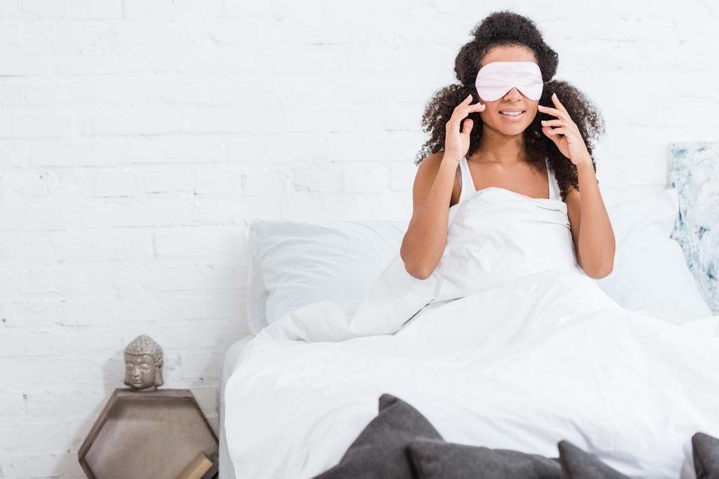 african american girl with eyes covered by sleeping blindfold in bed during morning time at home - Photo, Image