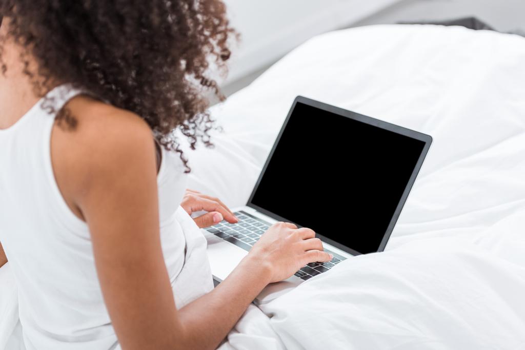 Μερική άποψη του σγουρά κορίτσι που χρησιμοποιούν φορητό υπολογιστή με κενή οθόνη στο κρεβάτι κατά τη διάρκεια του χρόνου το πρωί στο σπίτι - Φωτογραφία, εικόνα