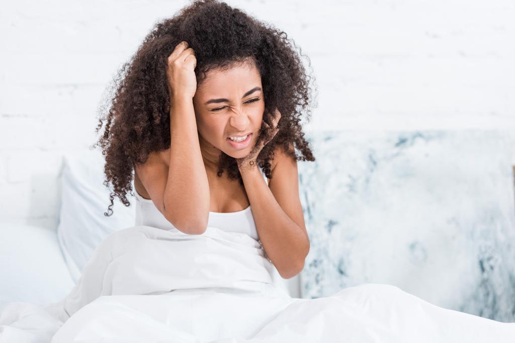 rizado joven afroamericana mujer teniendo dolor de cabeza en la cama en casa
 - Foto, imagen