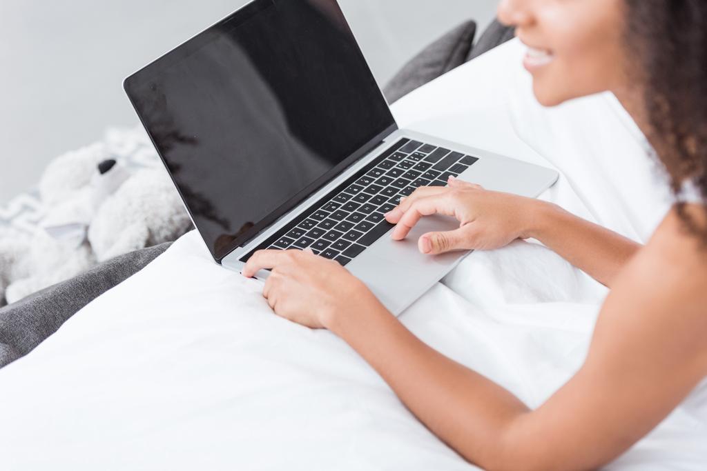 vista parcial de la mujer usando el ordenador portátil con la pantalla en blanco en la cama durante la mañana en casa
 - Foto, Imagen