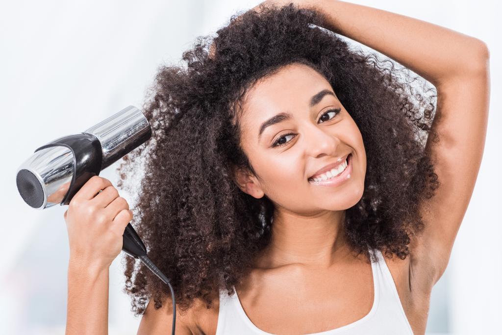 портрет кудрявой красивой африканской девушки, сушащей волосы дома
 - Фото, изображение