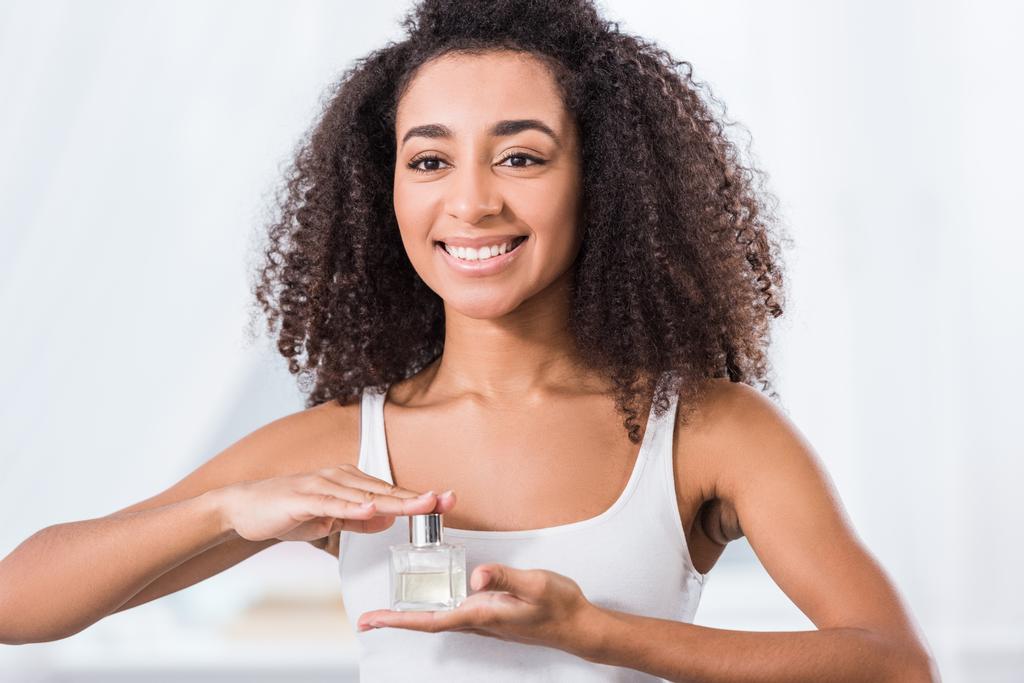 laughing young woman with curly hair holding perfume bottle  - Photo, Image