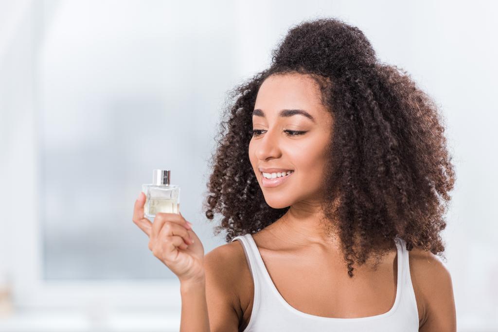 happy african american curly girl using perfume at home - Photo, Image