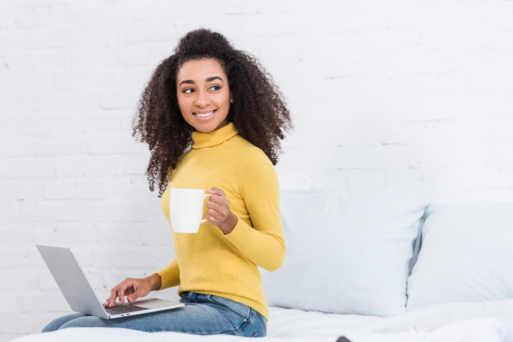 lockige afrikanisch-amerikanische Freiberuflerin mit Kaffeetasse, die zu Hause am Laptop arbeitet - Foto, Bild