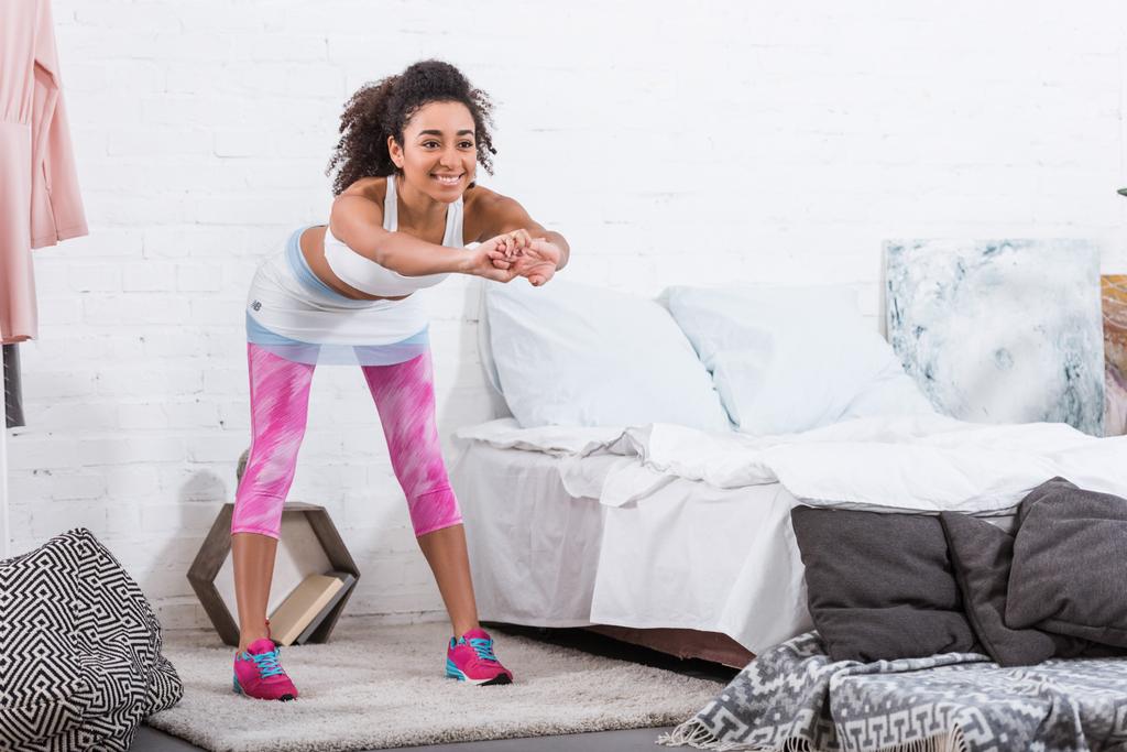 vrolijke african american vrouw doen oefening in ochtend tijd in slaapkamer thuis - Foto, afbeelding