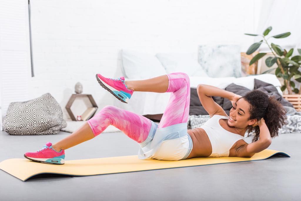 usmívající se africká americká sportovkyně dělá abs na fitness mat v ložnici doma - Fotografie, Obrázek