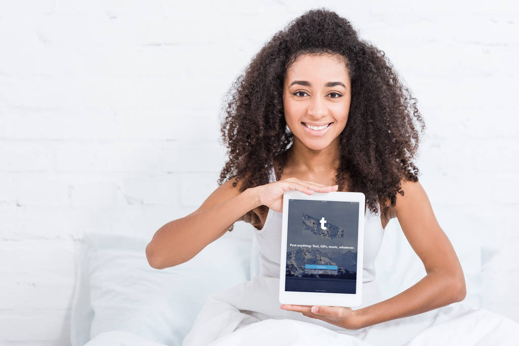 Happy americkou afričanku zobrazeno digitální tablet s tumblr na obrazovce v posteli doma - Fotografie, Obrázek
