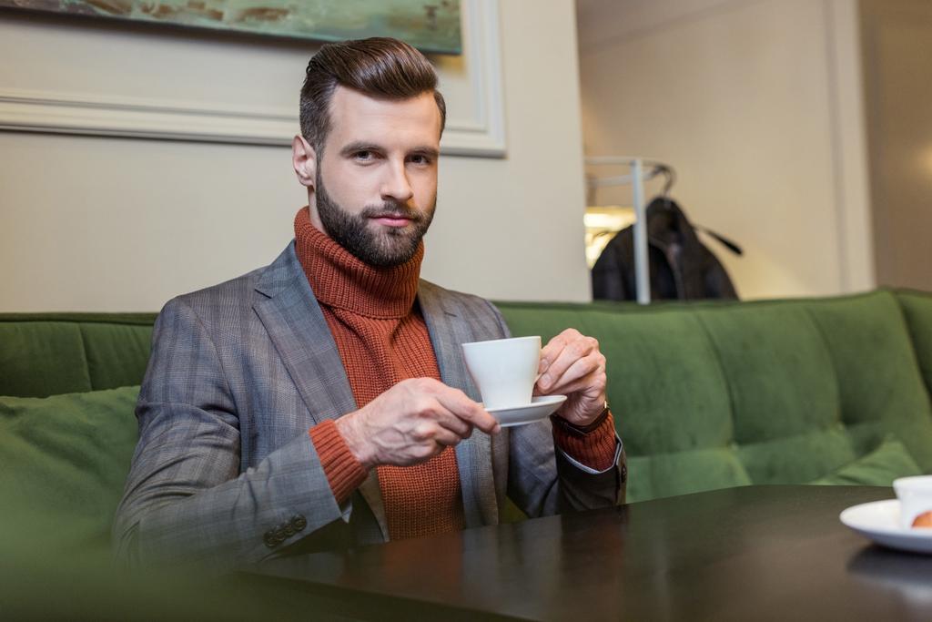 yakışıklı adam kameraya bakarak, masada oturan ve restoranda kahve içme formal giyim - Fotoğraf, Görsel