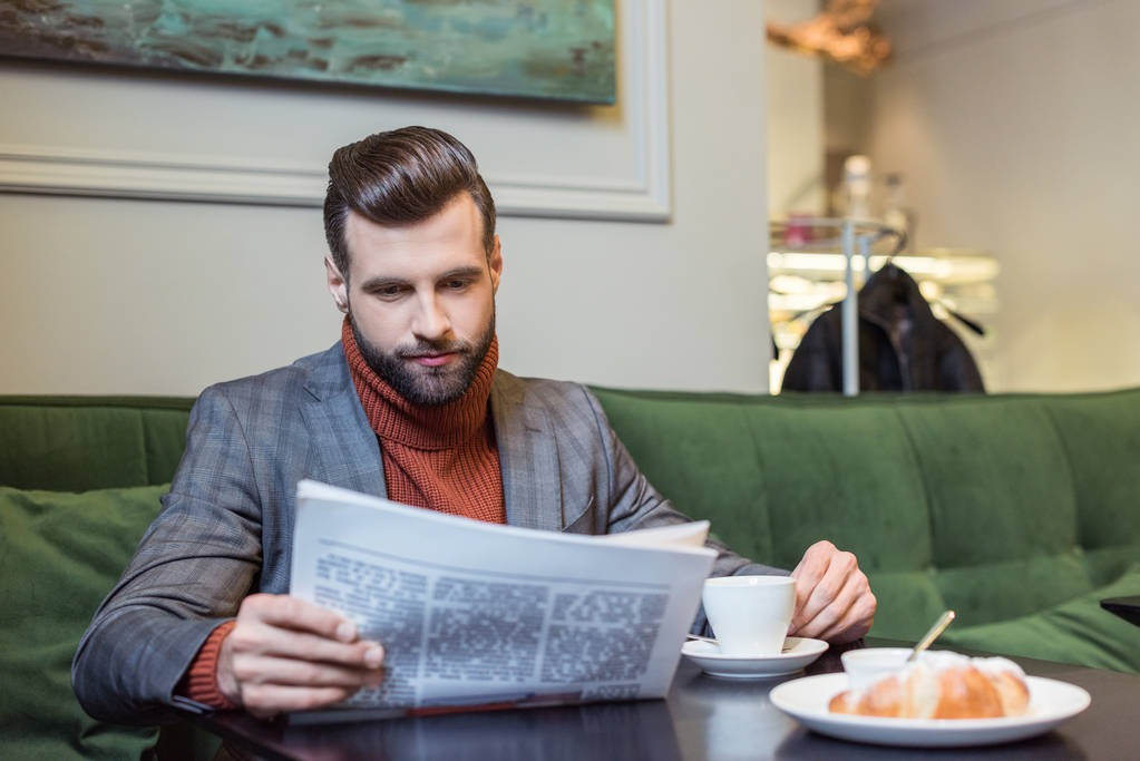 Stylowy mężczyzna w wizytowym siedzi przy stole z kawą i czytanie gazety w restauracji  - Zdjęcie, obraz