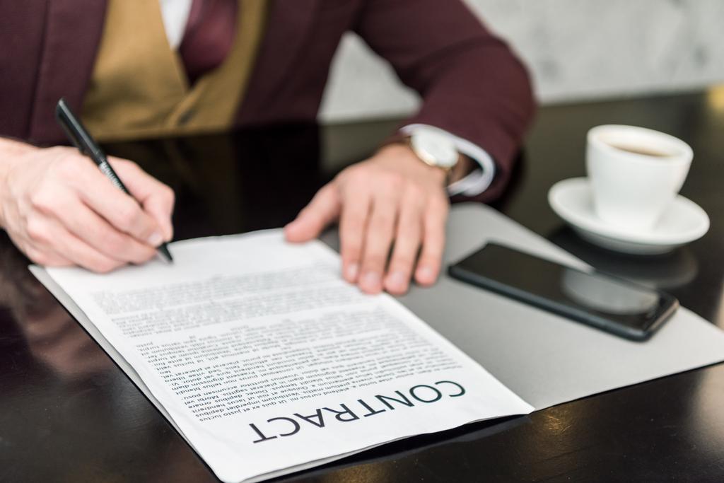 обрізаний вид бізнесмена в офіційному одязі, що сидить за столом і підписує контракт
  - Фото, зображення