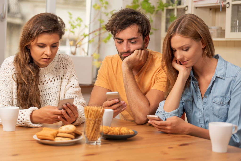 Mutfakta oturuyor ve üstünde onların telefon izlerken arkadaşlar. Internet'te gezinme ve teknoloji bağımlılığı kavramı - Fotoğraf, Görsel