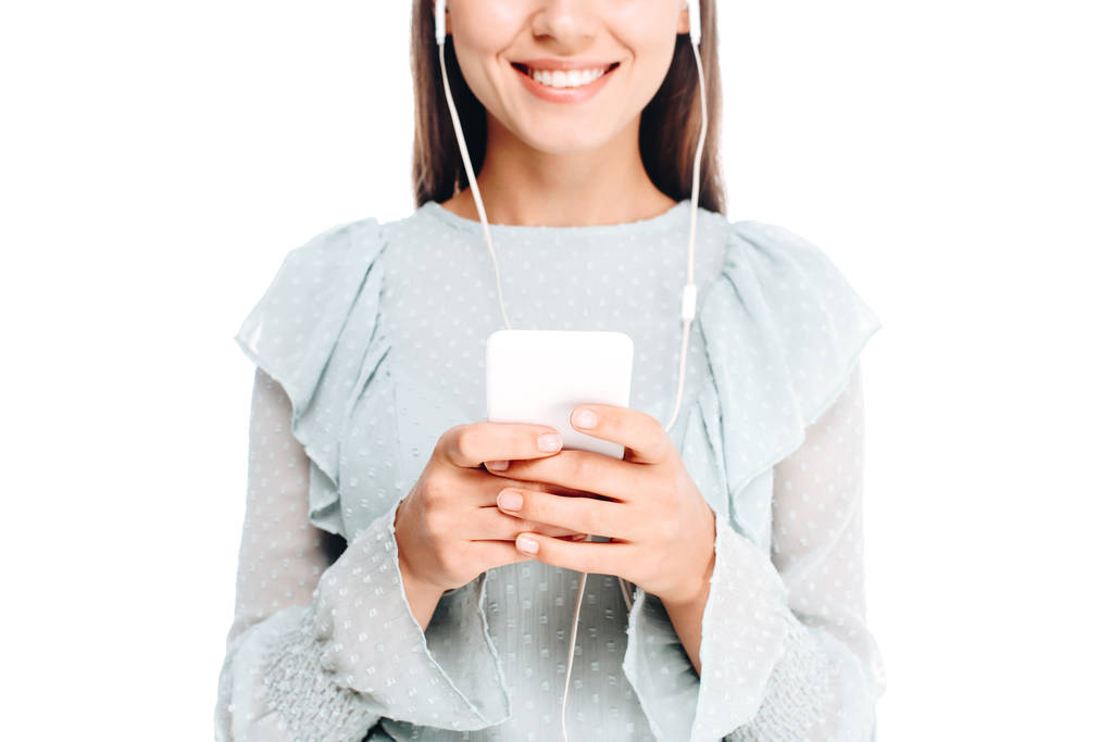 przycięte strzał uśmiechający się kobiety za pomocą smartfonu, podczas słuchania muzyki w słuchawkach na białym tle - Zdjęcie, obraz