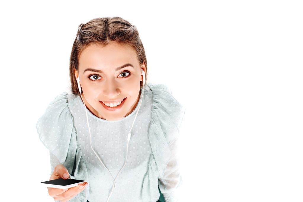 vista de ángulo alto de la mujer sonriente con teléfono inteligente escuchar música en auriculares aislados en blanco
 - Foto, Imagen